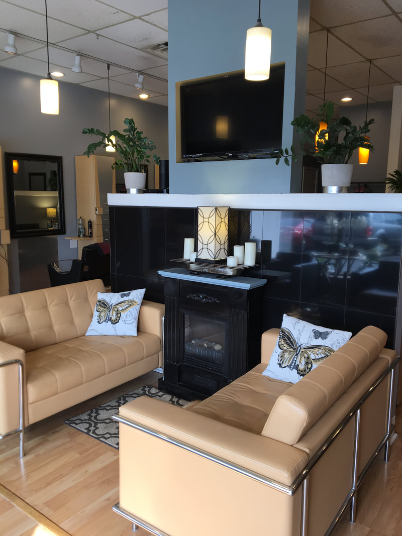The Vina Salon waiting area: two tan leather sofas, a candlelit fireplace and pendant lights