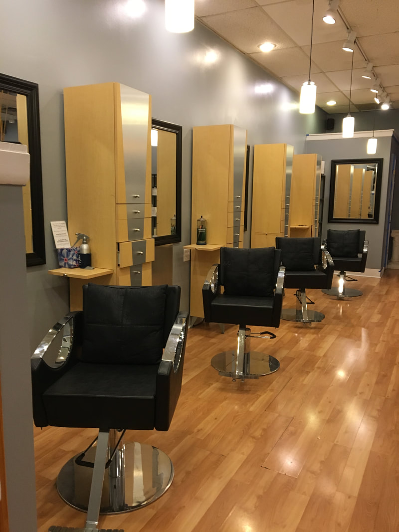 A row of black styling chairs and wood stations with mirrors inside Vina Salon